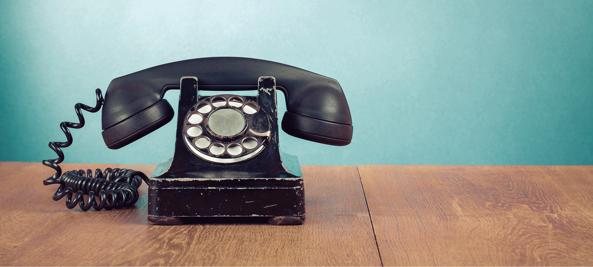 An Old school rotary dial phone on a table.